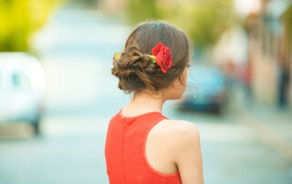 back view of girl with roses in stylish hair and summer dress posing on sunny day on blurred background. Hairdressing salon