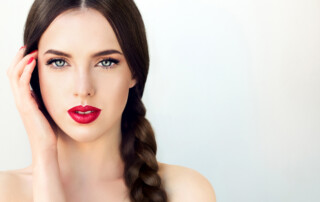 Close up portrait of beautiful young brunette woman-model with long braided hair. Pigtail hairstyle. Bright blue eyes, red lipstick on the lips and red manicure on the nails.